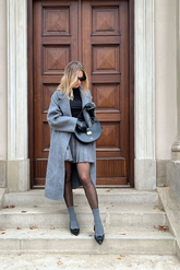 a lady in a black top,  a grey long wool coat and a grey pleated skirt